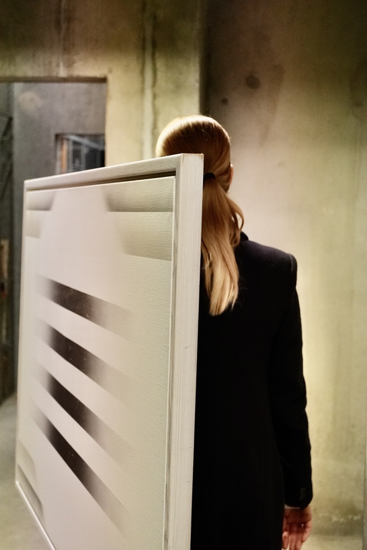 Annemette Müller bærer et stort maleri af Finn Mickelborg, akryl på lærred, i en kældergang.